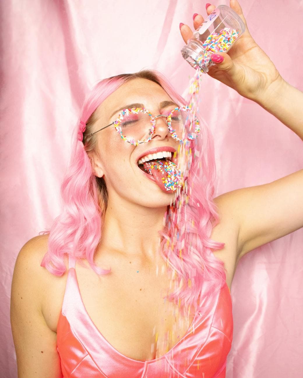 Creator with pink hair celebrating as she pours rainbow sprinkles